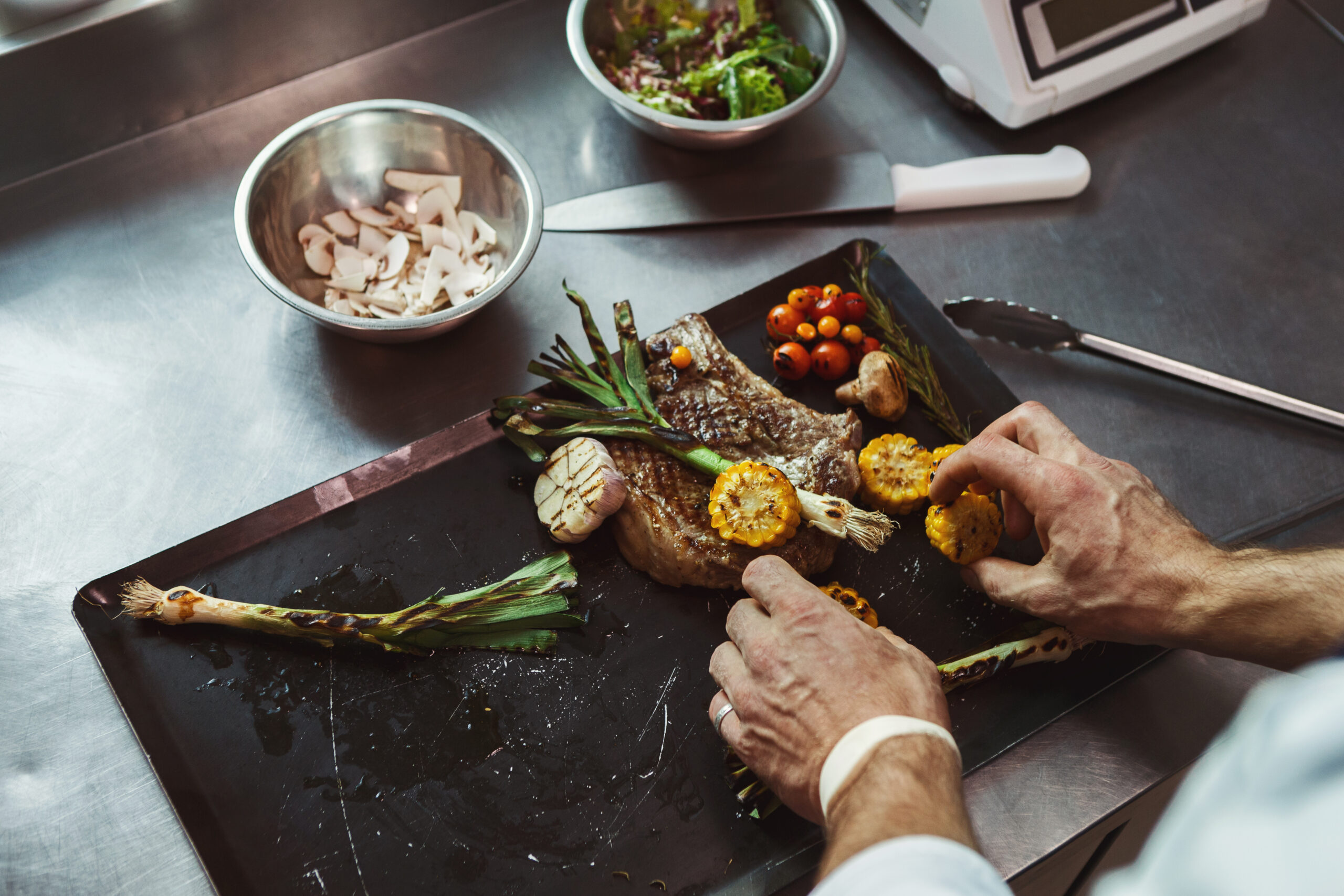 Male chef cooking and serving juicy medium beef steak and grilled vegetables. Healthy exclusive food prepared at professional kithen