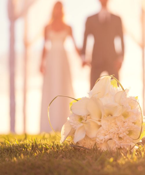 Close up of Wedding Bouquet. Focus on Flowers. Bride and Groom in Background.